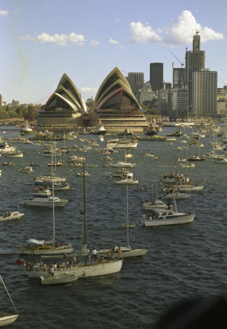 The Sydney Opera House and Sydney skyline as seen on the day of the Sydney Opera House's opening. Pleasure craft dot the harbour.
