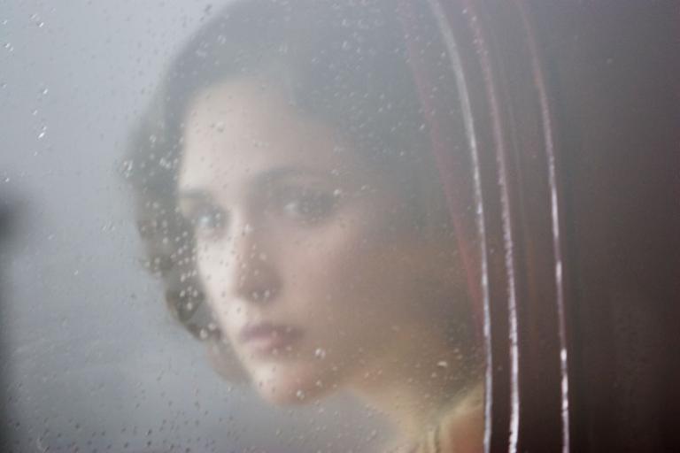 Rose Byrne as Iris in The Tender Hook, looks out a window that is fogged over and covered in raindrops.