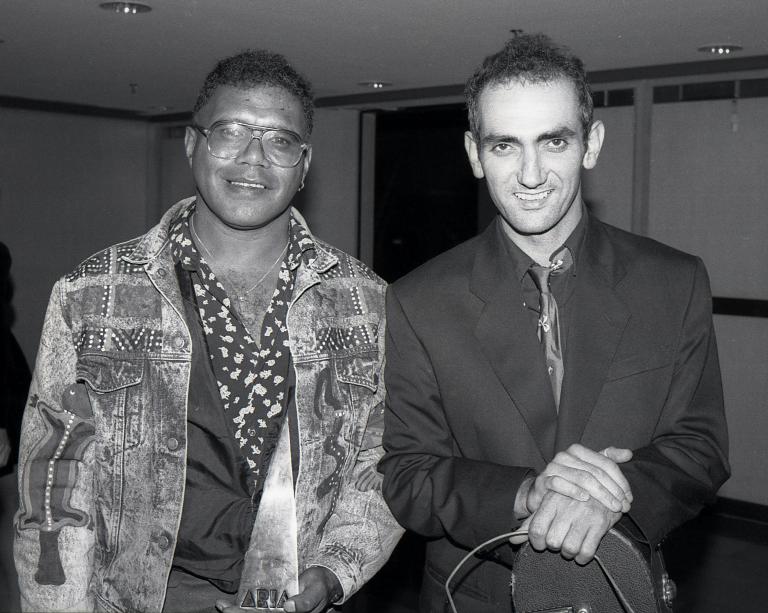 Archie Roach and Paul Kelly A black and white photograph of Archie Roach and Paul Kelly. Archie holds an ARIA award in his hand. They are both smiling.