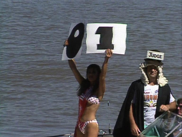 Girl in a bikini holds up a sign with the numbers 0 and 1, on Lake Burley Griffin