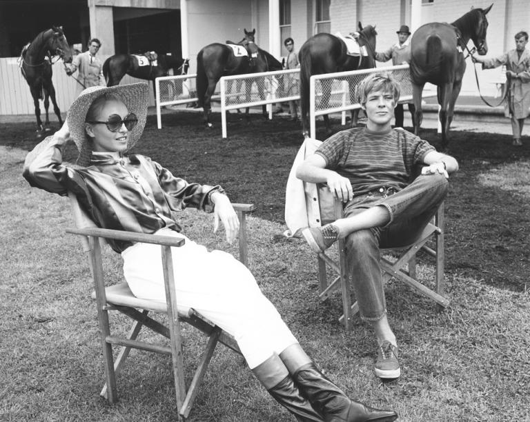 Two actors sitting on folding chairs with horses in the background.