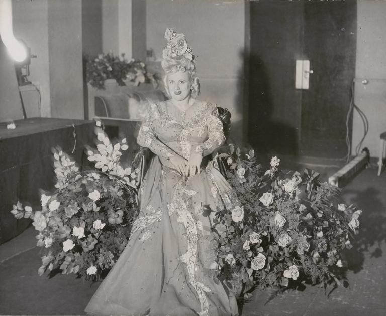 Marjorie Lawrence wearing an exotic dress and surrounded by flowers.