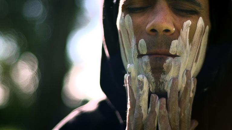 Indigenous man wipes white clay onto his face. Indigenous man wipes white clay onto his face.