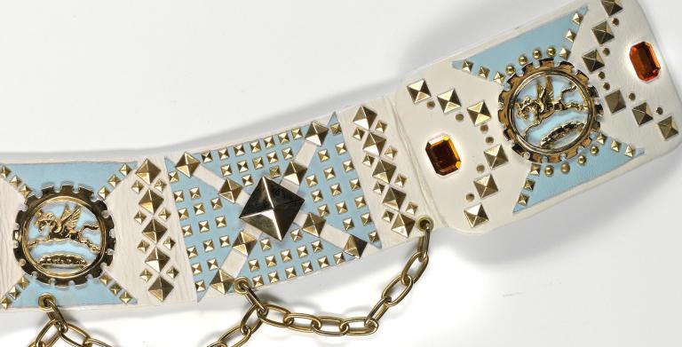 A blue and white belt decorated in rhinestones, studs and gold chains. The belt is part of a costume made for the film ELVIS.