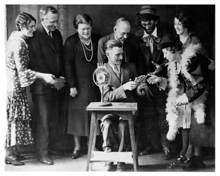 A group of people standing around a man seated at a small table behind a 2UE microphone