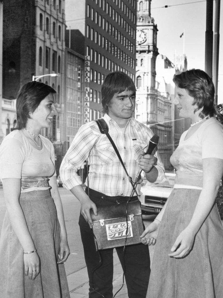 A man with a portable tape recorder in a satchel and holding a microphone interviews two women on the streets of Melbourne in the 1970s.