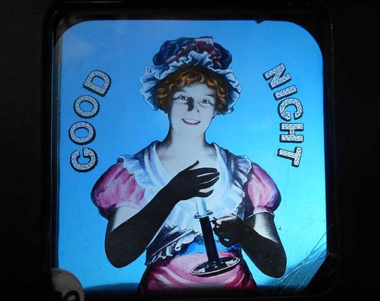 A glass slide with an image of a young woman holding a candle and smiling. The words 'GOOD NIGHT' are written on the slide.