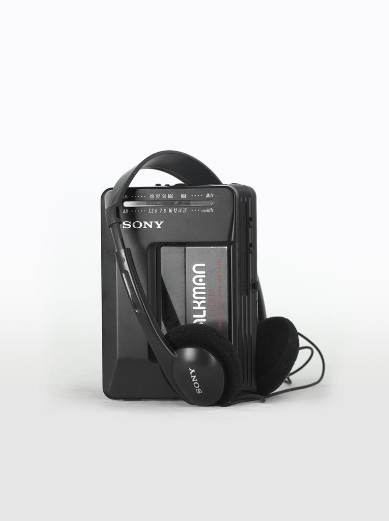 A black Sony Walkman portable radio and cassette player with headphones sitting on top of it.