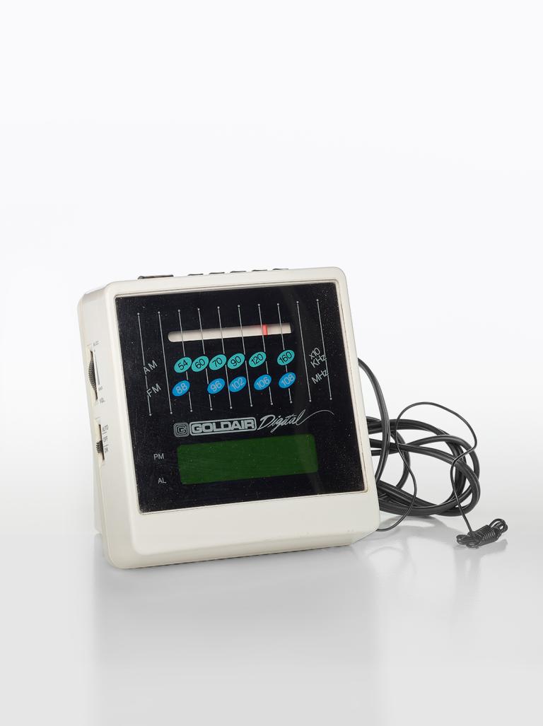 A digital clock radio from the late 1970s with AM and FM bands on the front, knobs on the side and an electric cord.