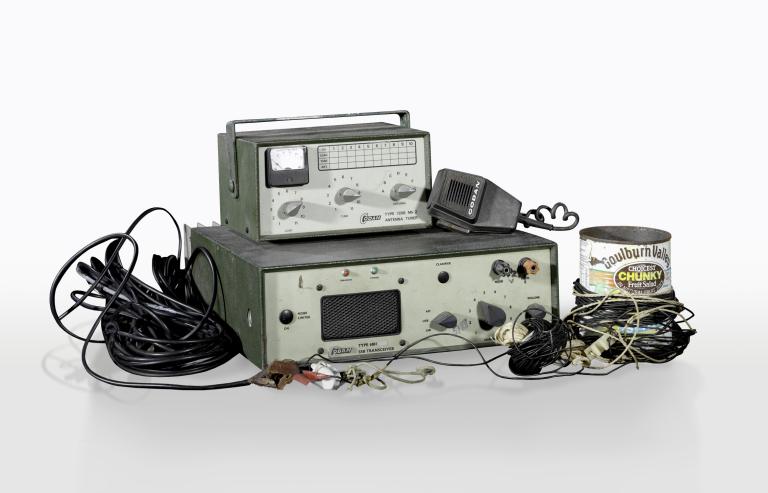 A collection of homemade radio equipment including a transceiver box with knobs and speaker, an antenna tuner, cords and a fruit salad tin used as an antenna.