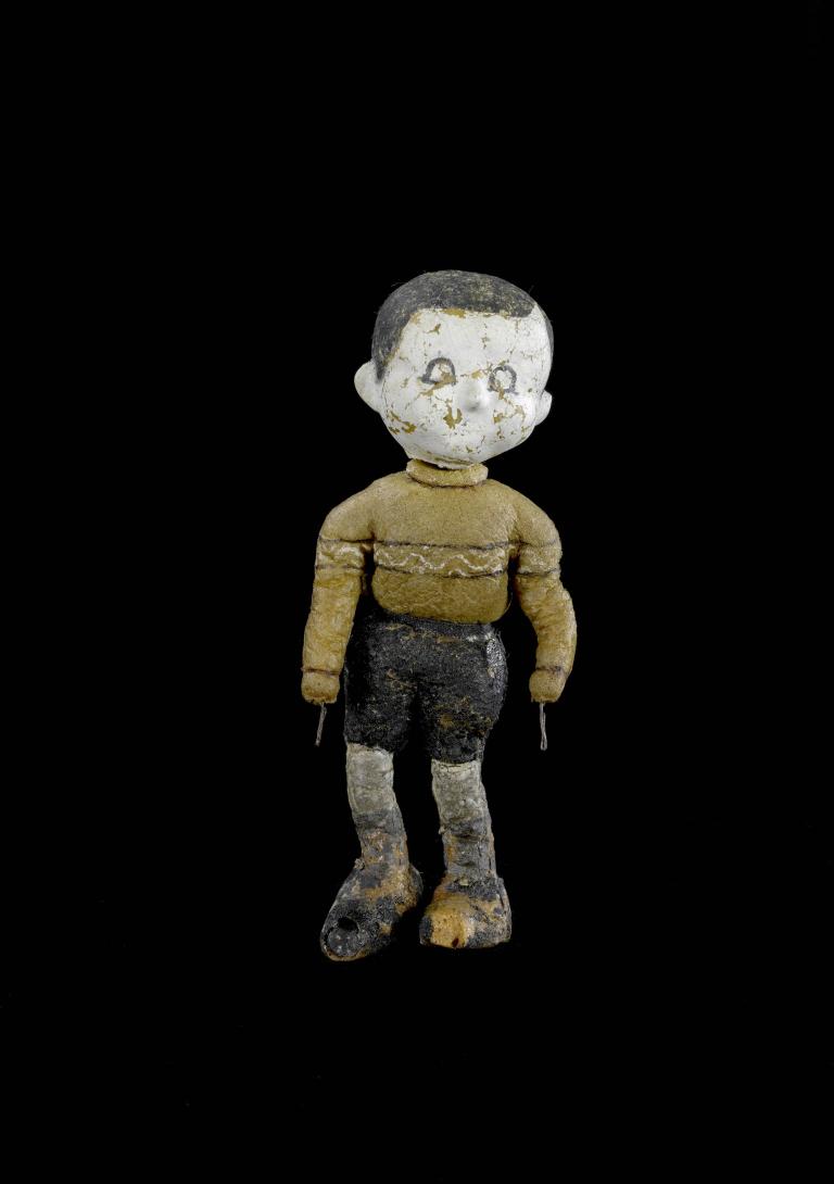 A photo of a small puppet. It is wearing a yellow jersey and black shorts.