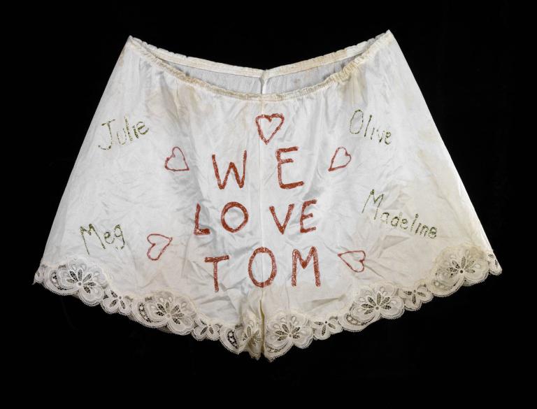 A photo of lacy underwear in which "We Love Tom" is written with red stitching.