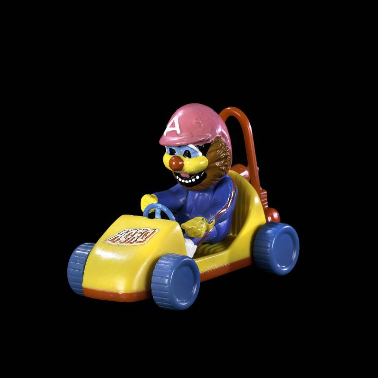 A photo of Argo in a yellow toy car with blue wheels. Argo is wearing a pink racing cap with the letter A on it. 
