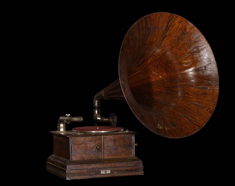 A photo of a gramophone against a black background. The trumpet and box of the gramophone are both wood textured.
