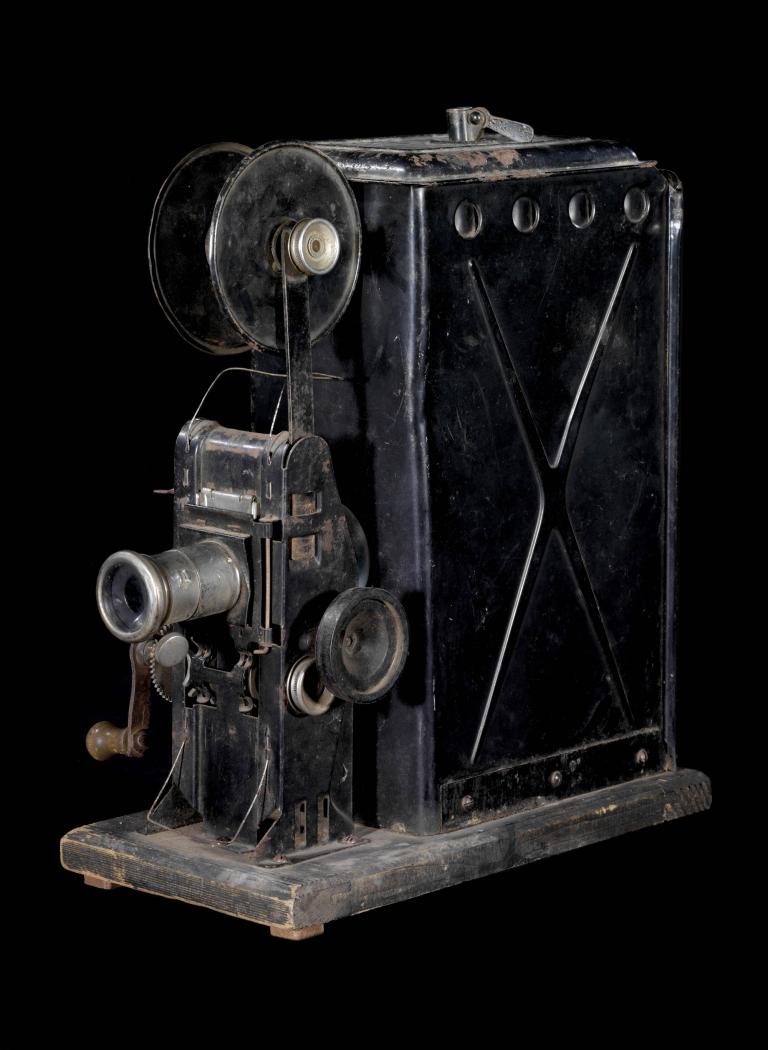 A photo of a black projector with a lens at the front connected to a large black box at the back. 