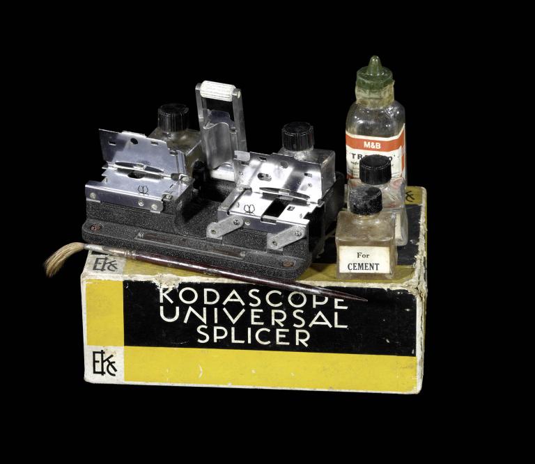 A photo of a splicer which sits on top of its box that reads "Rodascope Universal Splicer". On top of the box is a small kit with three bottles.
