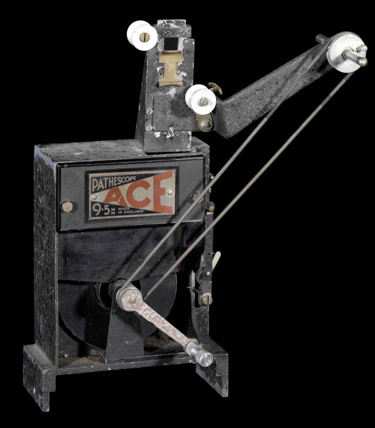 A photo of a film projector. It is black in colour with the Pathescope Ace logo label on the side.