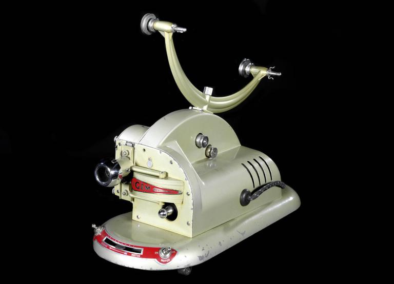 A photo of a film projector. It's beige in colour with black dials and a few decorative red highlights.