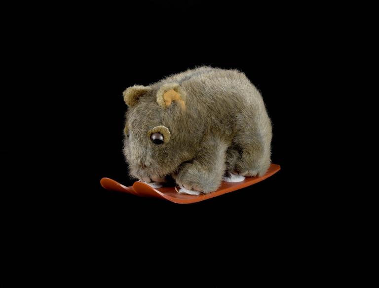 A photo of a toy wombat on red skis.