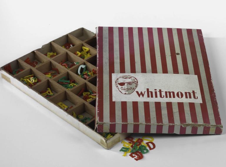 A photo of an open box. The cover has red and white strips and the Whitmont Logo on it. Inside the box it is divided into rows of 5 with letters to create your own end titles. 