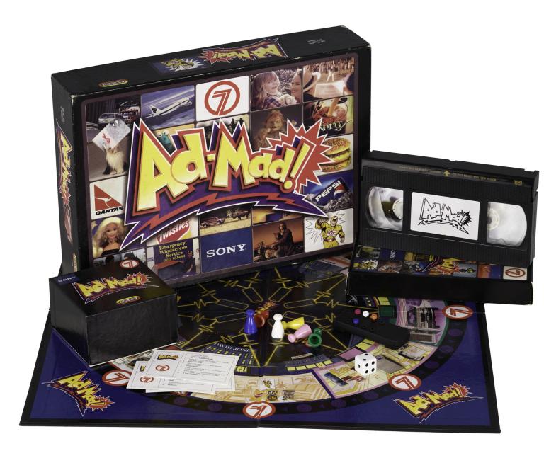 Ad Mad! board game components including the VHS tape, colorful playing pieces, dice, and game cards arranged together