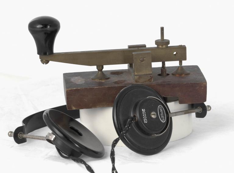Vintage Morse key and headphones from 1935, featuring a metal base, wooden knob, black wiring, and dials
