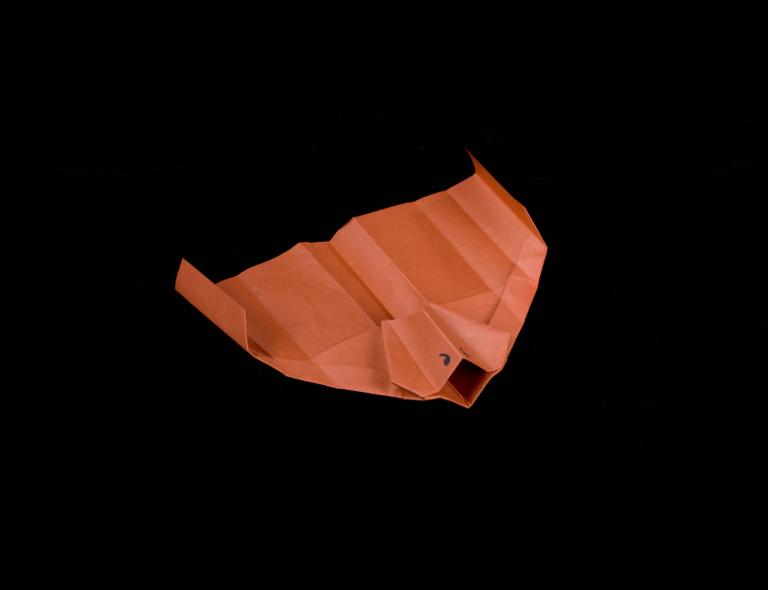 Orange paper plane on a black background, folded and shaped.