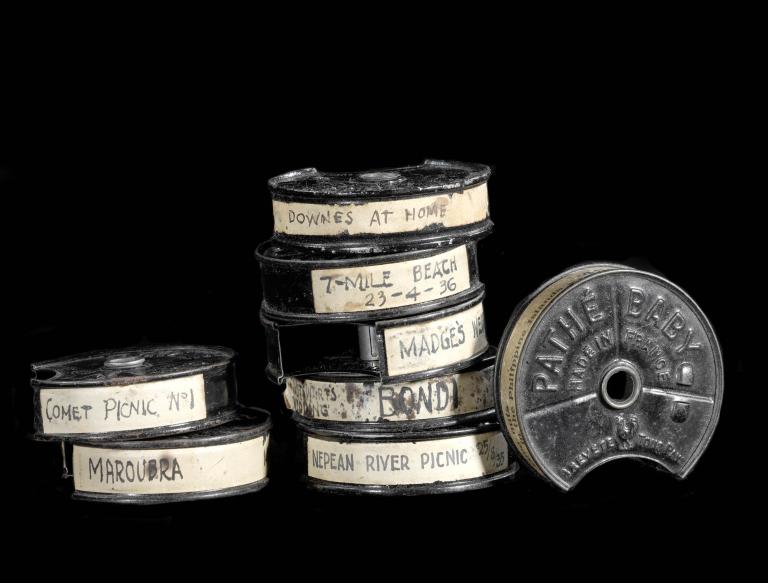 Stack of vintage Pathe Baby 9.5mm film reels with handwritten labels against a black background