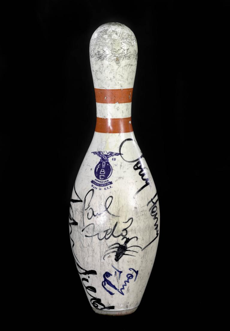 Signed bowling pin with celebrity autographs on a black background