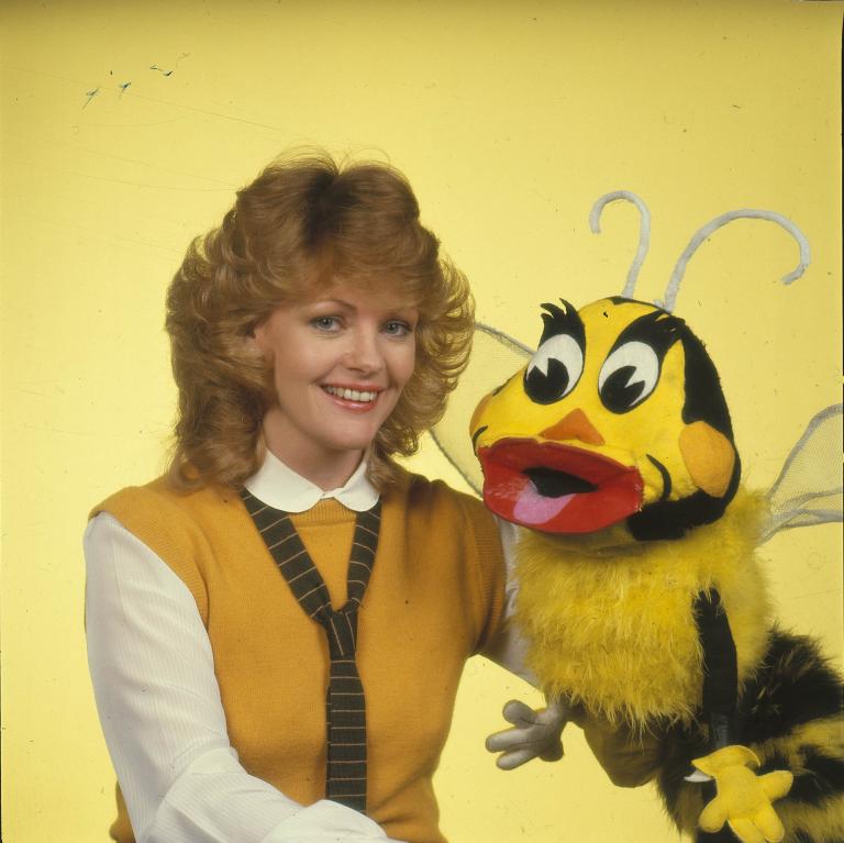 Miss Helena smiling next to a bee puppet from a 1980s Australian children's TV show.