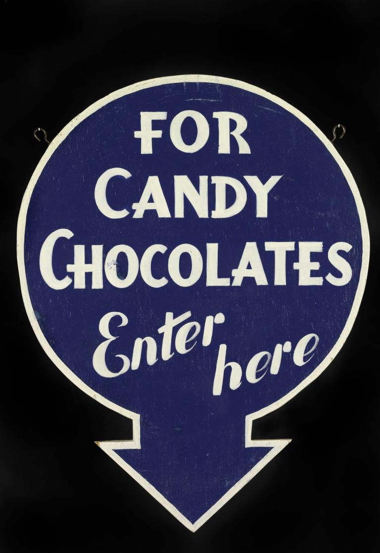 Blue sign with white text reading 'For Candy Chocolates Enter here,' featuring a downward arrow