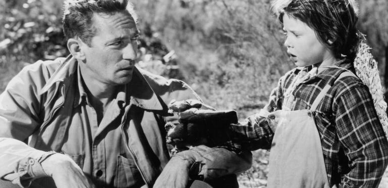 Peter Finch sitting on the ground holding his hat talking to a child
