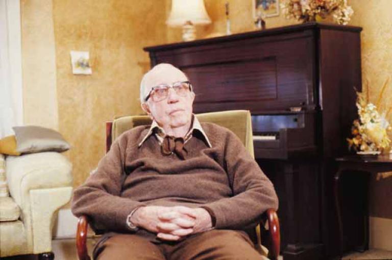 Singer Jack O'Hagan is sitting in an armchair in a home with a piano in the background.