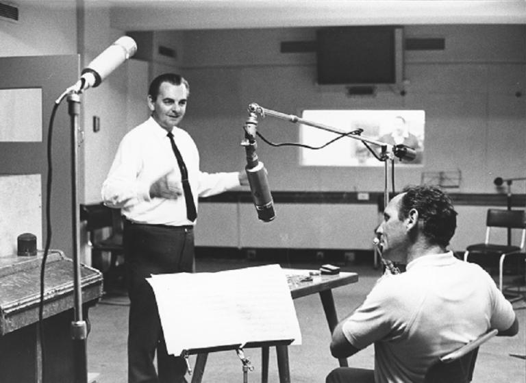 Eric Jupp standing while Don Burrows plays the flute in a recording studio.