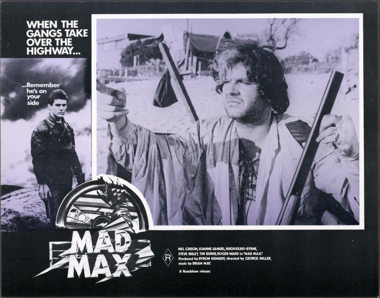 Lobby card for Max Max shows Toecutter (Hugh Keays-Byrne) pointing and holding a rifle.