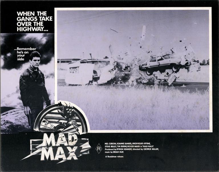 Max Max 1 lobby card shows a car flying through the air and smashing though a caravan.