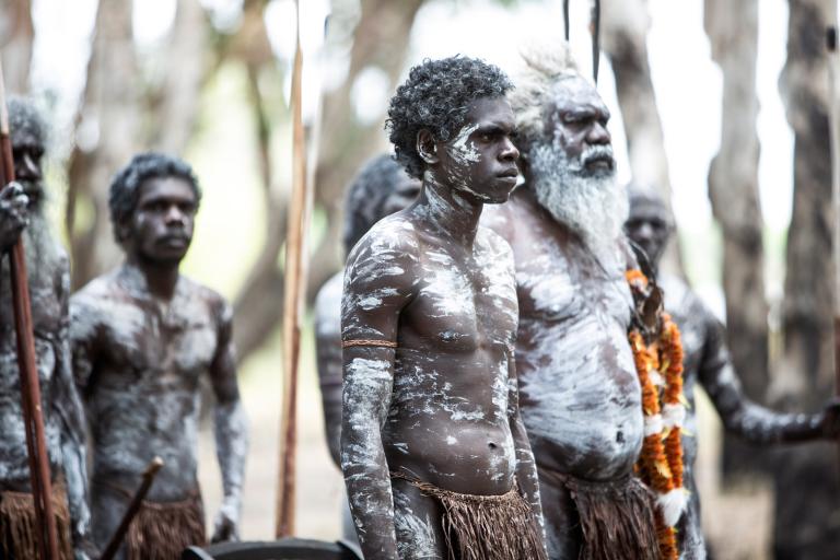 A group of Aboriginal men in the bush wearing traditional body and face paint.