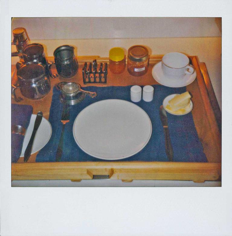 Polaroid of Graham Kennedy's wooden breakfast tray showing plates, cutlery, salt, pepper, cup and saucer, teapot, tea strainer, toast stand, butter dish and other items.