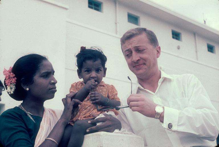 Graham Kennedy in India with a young mother and her baby girl. The baby girl is chewing on Graham's glasses.