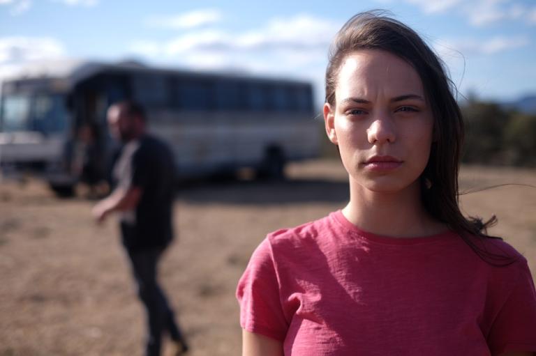 A woman close up to the camera with a man and bus in the background.