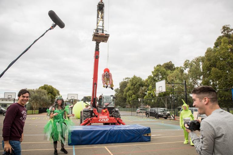 Crew on set. A clown is suspended from a crane.