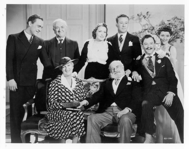 The cast from the film Dad and Dave come to town, seated on and standing around a sofa, smiling at camera.
