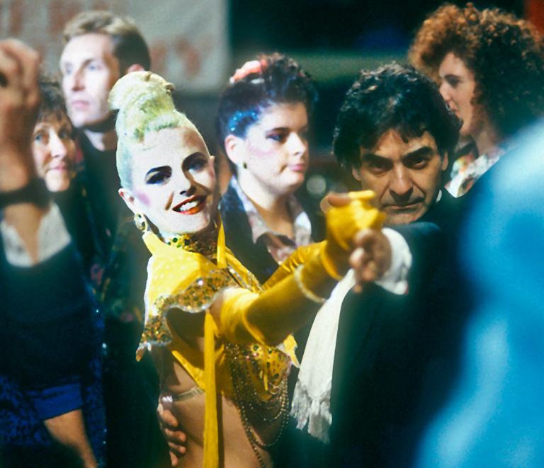 A young woman dances with a middle aged man in a tuxedo in the middle of a crowd. 