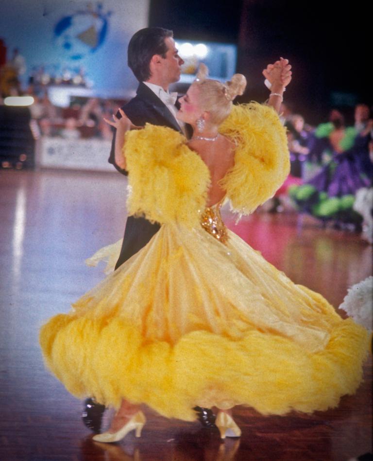 A man in a black tuxedo dancing with a woman in a yellow ballroom gown.