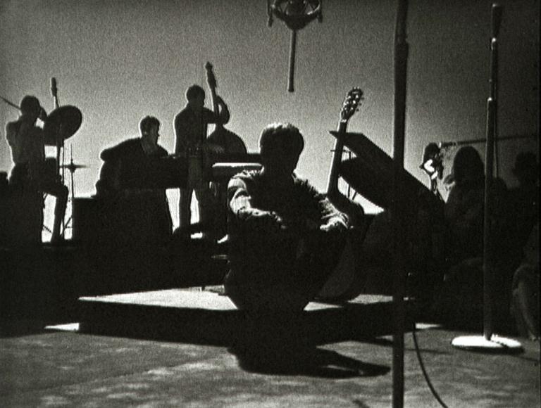 Tony Cole on the set of music television show 'Boomeride' sitting in darkness with his backing band behind him.