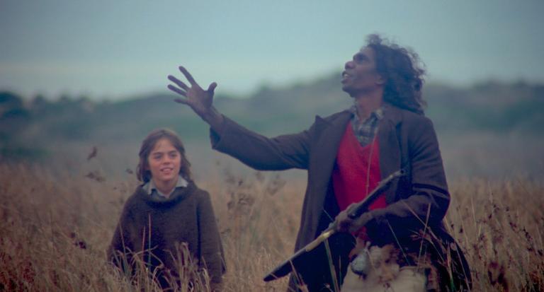 David Gulpilil as Fingerbone Bill and Greg Rowe as Storm Boy standing together. Fingerbone Bill is gesticulating up into the sky. He's holding a gun.
