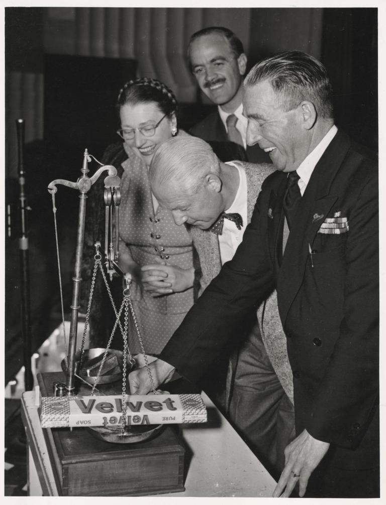A woman and three men looking at a large bar of soap on a scale