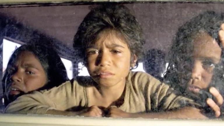 Three Aboriginal girls stare out the back window of a car having just been taken from their mothers