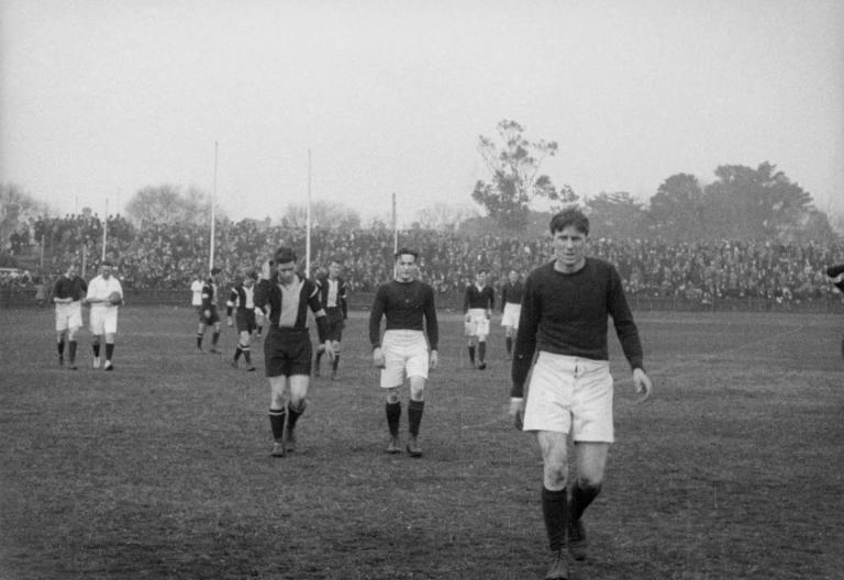 AFL players walking off of a field with cutaways to cheering crowds.
