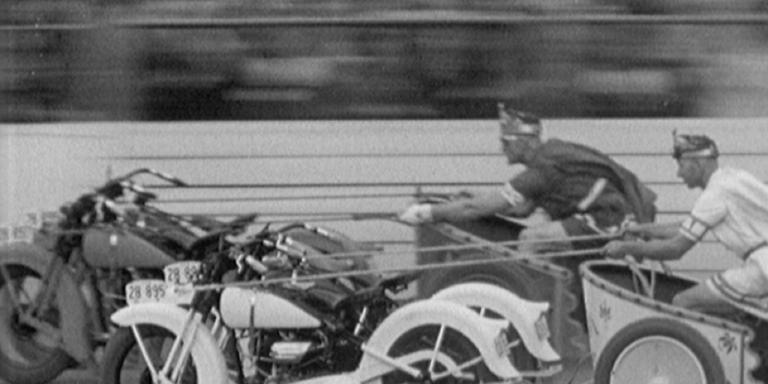 Two police officers in costume, riding their 'motorcycle chariots', Ben Hur style